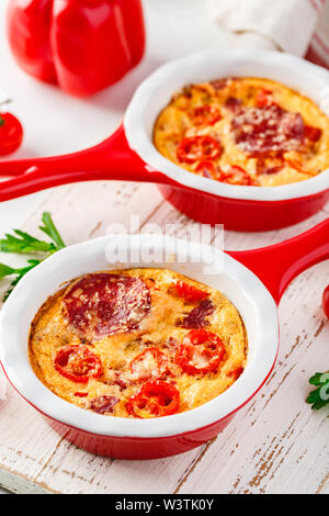 Frittata aux poivrons doux frais, tomates et de salami. Omelette italienne en céramique rouge poêlons sur un fond blanc. Close up Banque D'Images