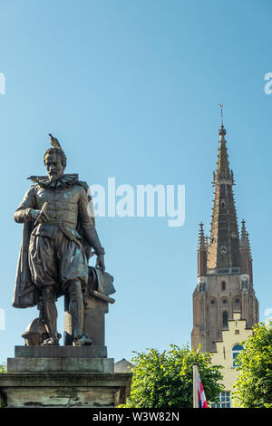 Bruges, Flandre occidentale, Belgique - 17 juin 2019 : Simon Stevin statue avec flèche de OLV Cathédrale en arrière sous ciel bleu. Feuillage vert certains. Pigeon sur son Banque D'Images