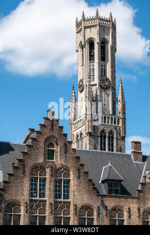 Bruges, Flandre occidentale, Belgique - 17 juin 2019 : pierre gris tour de beffroi avec réveil brique brune peeps sur l'étape gable sous ciel bleu avec whtie cloud. Banque D'Images