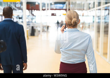 Businesswoman talking on mobile phone while walking in corridor Banque D'Images