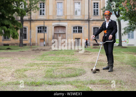 16 juillet 2019, Saxe, Wermsdorf : Action Artiste Ralf Witthaus se distingue avec un motorsense dans l'ancien jardin baroque dans le parc du château de Hubertusburg. Le plus grand pavillon de chasse a retourné une fraction de son jardin perdu. Avec environ 40 bénévoles, l'action de Cologne artiste a cut gratuitement quelques-unes des formes de bijoux dans l'ancien parc depuis le 1er juillet. Sur 10 000 mètres carrés, l'axe central et le centre du jardin baroque composition ont été ressuscités - un dixième de l'ancien complexe. Mais les visiteurs à l'axone 'Versailles' faut se dépêcher, parce que c'est un travail temporaire. Banque D'Images