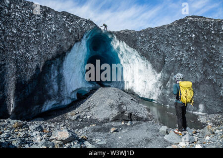 Deux guides à un énorme caverne de glace sur le Glacier Matanuska en Alaska. Avant d'entrer dans la grotte, un guide sur le haut renverse les roches qui peuvent fal Banque D'Images