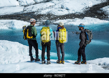 Quatre ice climbers ensemble permanent sur la Matanuska Glacier et un lac supraglaciaire sur le dessus de la glace du glacier blanc. Banque D'Images