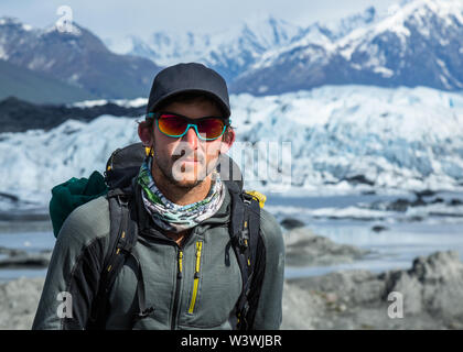 Un homme dans un chapeau et des lunettes à billes avec un sac à dos se trouve en face d'un glacier en Alaska à distance. Il est un guide, réunissant des gens hors de l'escalade de glace sur un gl Banque D'Images