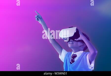 Image composite de l'écolier le port de casque de réalité virtuelle pointant avec bras levés Banque D'Images