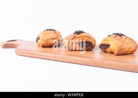 Trois des petits rouleaux de pâte feuilletée remplie de chocolat sur une planche en bois sur fond blanc Banque D'Images