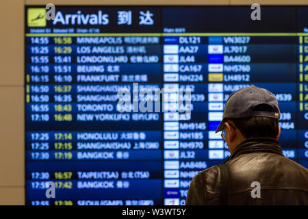 Un homme en casquette de baseball regarde le tableau des arrivées de l'aéroport international de Haneda à Tokyo, au Japon. Banque D'Images