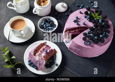 Blueberry et blackberry gâteau mousseline au fromage à la crème à l'intérieur sur un plat noir sur une table avec une tasse de thé, le lait dans un pichet et de baies dans un b Banque D'Images