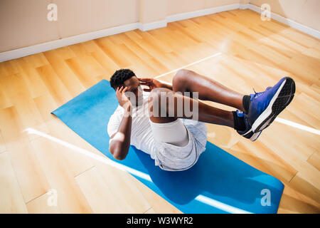 Vue de dessus de young African American man doing sit-up exercice sur tapis de yoga à la salle de sport. Remise en forme de la scène de sexe masculin modèle crunch au centre de remise en forme Banque D'Images