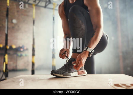 La préparation de l'entraînement. Photo recadrée de la belle jeune femme en vêtements de sport lier ses lacets tout en exerçant en salle de sport. Le sport professionnel. Formation TRX. Mode de vie sain Banque D'Images