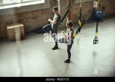 L'exercice ensemble. Jeune couple actif dans les jambes avec la formation de sport fitness Trx attaches, au sport. Entraîneur personnel. Formation TRX. Banque D'Images