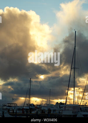 Coucher de soleil éclate de façon spectaculaire grâce à l'assombrissement de nuages de pluie plus de yachts dans la marina Banque D'Images