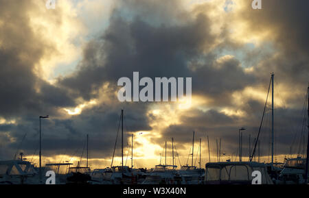 Coucher de soleil éclate de façon spectaculaire grâce à l'assombrissement de nuages de pluie plus de yachts amarrés en toute sécurité dans une marina Banque D'Images