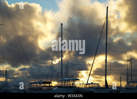 Coucher de soleil éclate de façon spectaculaire grâce à l'assombrissement des nuages de pluie sur les mâts et les sommets des yachts dans une marina sur la côte de Perth Banque D'Images