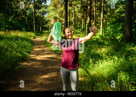 Woman taking photo avec sac à déchets en forêt. Après la collecte des ordures à la course à pied. Concept Plogging Banque D'Images