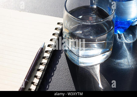 Verre d'eau près de pen allongé sur ouvrir le bloc-notes Banque D'Images