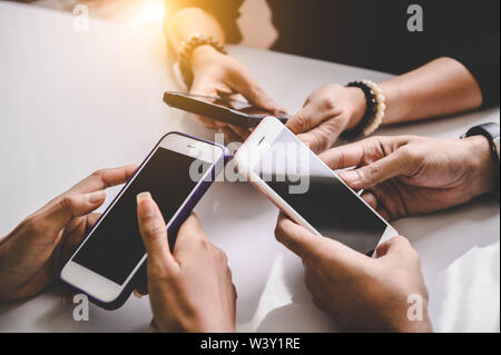 Groupe de jeunes hipsters holding phone dans les mains au bureau. Les amis de s'amuser ensemble avec les smartphones. La technologie et de la communication concept. Sc noir Banque D'Images