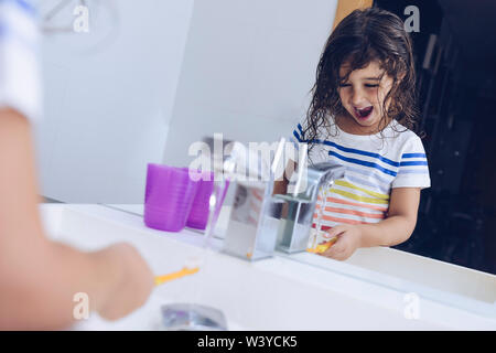 Funny little girl de mouiller la brosse à dents après avoir pris une douche, elle se prépare à se brosser les dents devant le miroir de la salle de bains, pour les enfants c'hygiène Banque D'Images