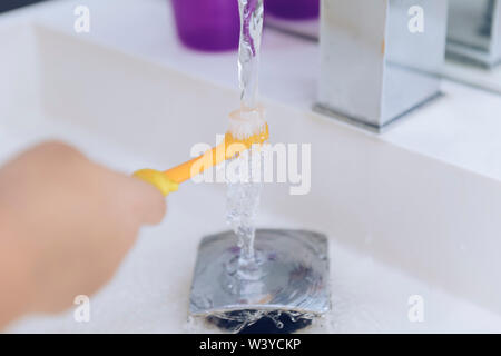 Main d'un enfant l'humidification de la brosse à dents, après avoir pris une douche elle se prépare à se brosser les dents, pour les enfants (concept d'hygiène Banque D'Images