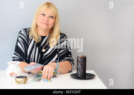 L'âge moyen belle femme est assise près d'un coin bureau avec un jeu de Tarot et des bougies. La lecture de carte. La divination et la voyance. Banque D'Images