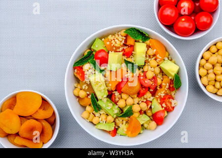 Bol déjeuner végétarien sain avec des fruits et légumes dont l'avocat, abricots, tomates, pois chiches et Boulgour Banque D'Images