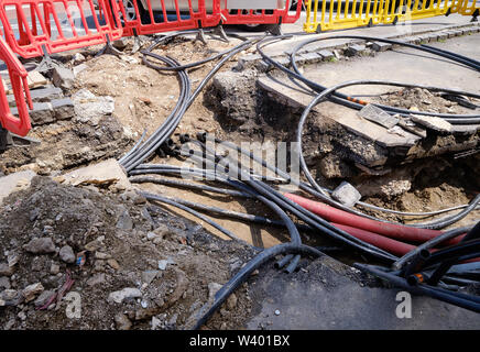 Creusé le trottoir révélant des fils dans des tubes de protection. Construction de lignes électriques ou de câbles de télécommunication, construction de connexions de réseaux optiques Banque D'Images