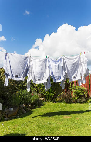 Shirts sèchent sur les lave-ligne dans UK jardin avec ciel bleu et nuages blancs moelleux. Banque D'Images