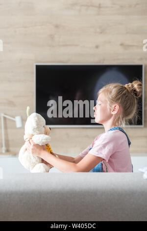 Belle petite fille sur canapé hugging teddy bear. Le concept d'une enfance heureuse, jeu dans la famille. Banque D'Images