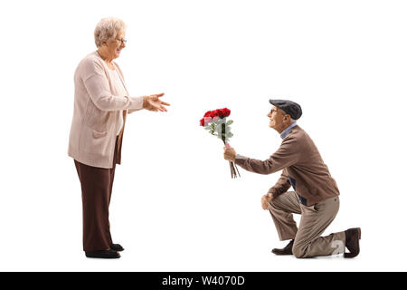 Longueur totale d'un homme à genoux hauts et donner un bouquet de roses rouges à un senior woman isolé sur fond blanc Banque D'Images