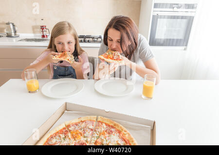 Mère et fille assis dans la cuisine, manger des pizzas et d'avoir du plaisir. Se concentrer sur sa fille Banque D'Images