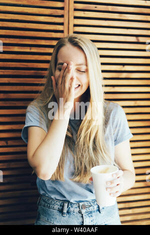 Un jeune blanc 30-year-old girl rire et lui couvre le visage avec sa main, émotions naturelles, le mode de vie. Cheerful woman with a paper Coffee cup sur un retour Banque D'Images