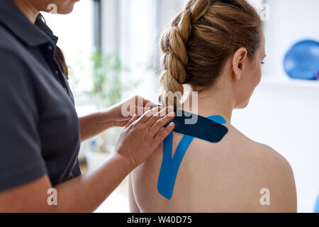 Femme chinoise massothérapeute appliquant kinesio tape pour les épaules et le cou d'une belle blonde client dans un bureau médical lumineux Banque D'Images