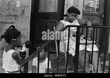 Mère afro-américaine des années 1960 et ses enfants, la fille joue avec une poupée blanche aux cheveux bouclés noirs. Mère écoute de la musique sur un tourne-disque portable, elle a sur ses genoux quelques disques simples, 45 tours par minute disques. Ils sont sur le porche de leur maison. Nouveau-Brunswick, New Jersey, 1969, USA années 60 US HOMER SYKES Banque D'Images