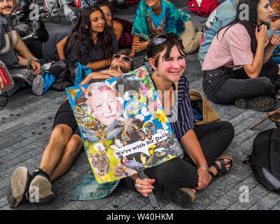 Londres, Royaume-Uni. 18 juillet 2019. L'Extinction d'un partisan de la rébellion est titulaire d'une plaque avec le message 'nous sommes avec Sir David' à l'Hôtel de Ville rassemblement et mourir à déclarer une grève de l'impôt contre l'Autorité du Grand Londres, l'élément de retenue d'AGL leur taxe d'habitation jusqu'à ce qu'ils abandonner des projets qui provoque la dégradation de l'environnement et de hâter l'effondrement écologique. Ils exigent la GLA arrêter tous les projets d'infrastructure et de l'air de Londres polluantes des investissements dans des mesures visant à réduire les émissions de carbone et d'encourager un mode de vie plus sain et à une assemblée de citoyens pour ré-écrire le Plan de Londres. Peter Marshall Banque D'Images