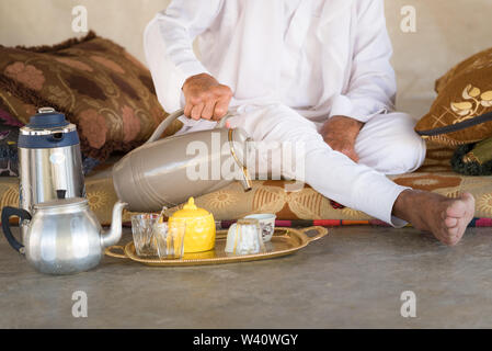 Bédouins arabes homme est assis sur le sol et se verse du thé ou du café à partir de la théière dans la tasse blanche en tente bédouine.arabe traditionnel blanc des vêtements. Banque D'Images