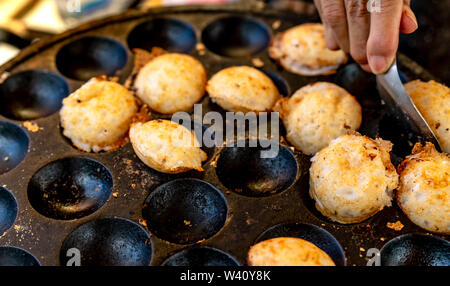 Grillé ou mortier-pâtisserie 'Kanom Krok' est un dessert traditionnel thaï. La femme dépose Kanom Krok de cuisinière en cuillère. L'alimentation de rue en Thaïlande. Thai Banque D'Images