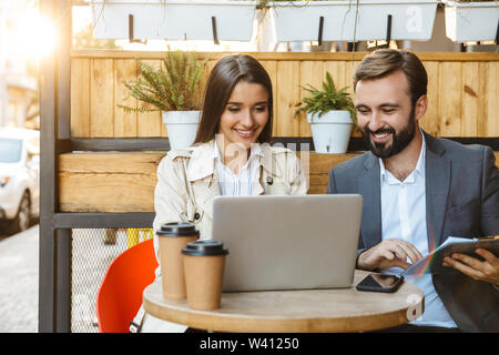 Portrait de l'heureux couple d'homme et de la femme de l'usure formelle avoir conversation et working on laptop ensemble tout en restant assis dans le café en plein air Banque D'Images