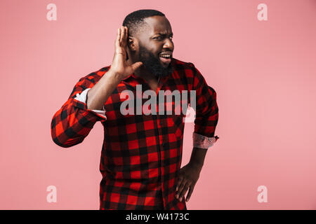 Portrait d'un agacé african man wearing plaid shirt isolés sur fond rose, gesticulant, essayant d'entendre des nouvelles Banque D'Images