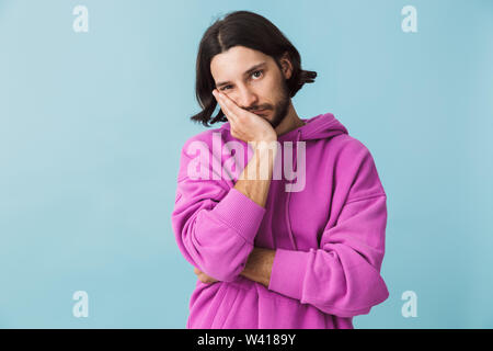 Portrait d'une jeune brunette barbu homme portant hoodie isolés sur fond bleu Banque D'Images