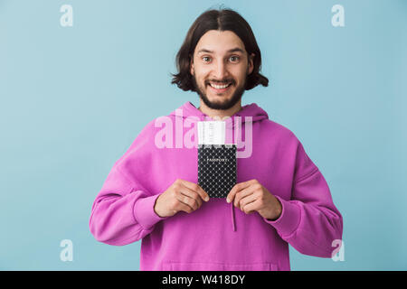 Portrait d'un jeune homme barbu portant des vêtements décontractés isolés plus de contexte, montrant passeport avec des billets de vol Banque D'Images