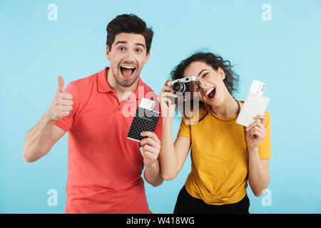 Cheerful young couple isolés sur fond bleu, avec des billets de vol de passeports montrant Banque D'Images