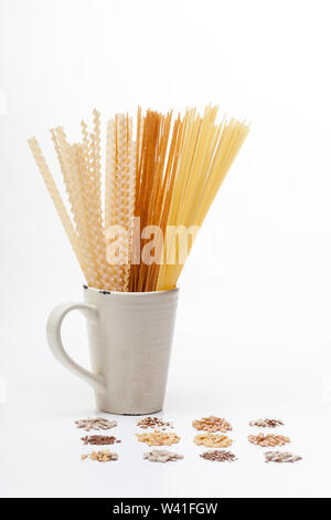 Mélange de pâtes crues et de la farine complète pâtes dans un tasse de porcelaine et une fourche avec collection de graines différentes on white Banque D'Images