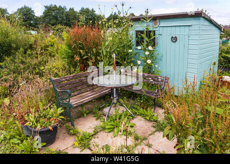 Vieux outils de jardinage de rouille et appuyé contre une cabane en bois qui est envahi par des buissons et fleurs sauvages, Sarajevo, Ayrshire, Scotland, UK Banque D'Images