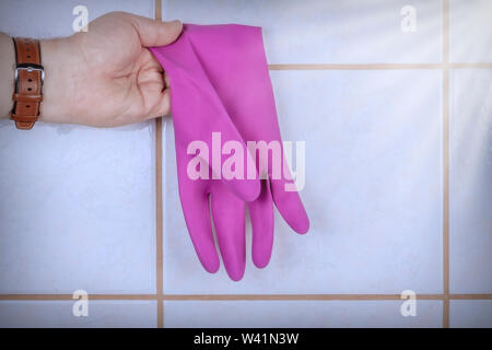 Main tient des gants en caoutchouc sur le fond des carreaux de céramique. Banque D'Images