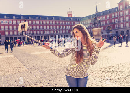 Belle jeune femme caucasienne heureux et excité sur la Plaza Mayor Madrid prendre une photo d'elle-même. À la joyeuse, poser et faire V-sign. En touri Banque D'Images