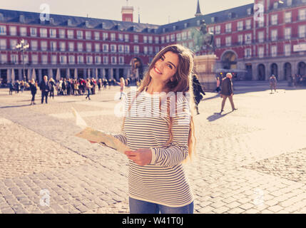 Belle jeune femme tourisme heureux et excité avec la carte d'essayer de trouver des lieux et monuments historiques sur la Plaza Mayor de Madrid, en Espagne, à la bonne humeur et la joie Banque D'Images