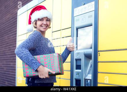 Femme avec santa christmas hat client utilisant le libre-service automatisé machine terminal post ou un casier pour déposer le colis pour le stockage Banque D'Images