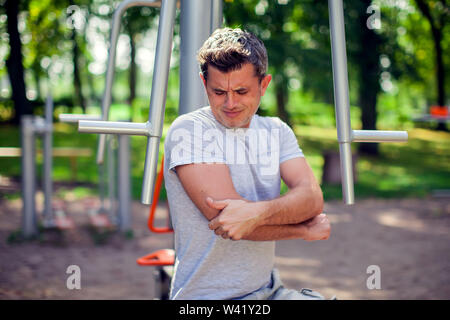 Un malheureux la sensation de douleur dans son coude pendant le sport et d'entraînement dans le parc. Le sport, la médecine et les gens concept Banque D'Images