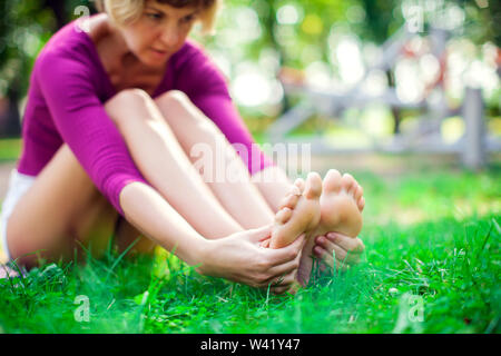 Jeune femme malheureuse ressentir la douleur dans son pied pendant le sport d'entraînement dans le parc. Le sport, la médecine et les gens concept Banque D'Images