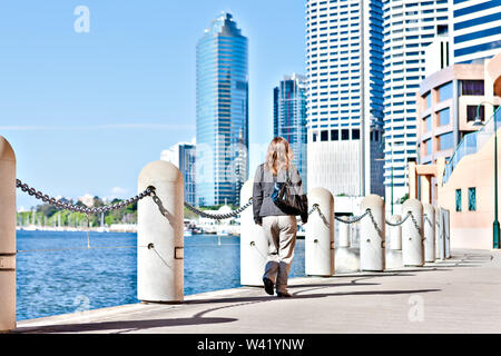 Vue arrière d'une femme marchant le long du sentier pédestre avec pilier en béton clôtures à côté de l'eau et la rivière bleue sous un ciel à partir de la ville de Brisbane, Queensland, au Banque D'Images